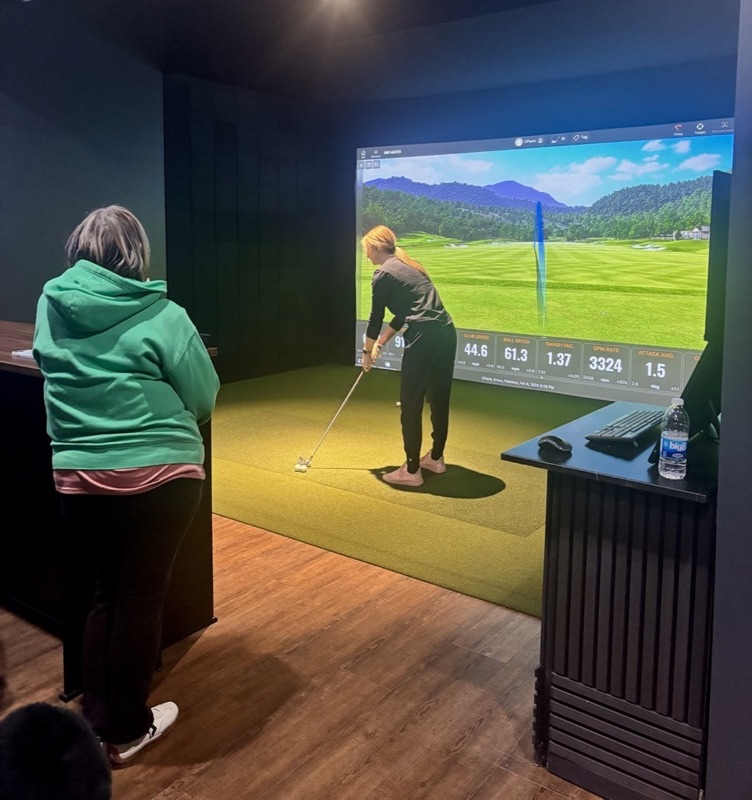 A golfer lining up an iron while a friend watches from the high-top