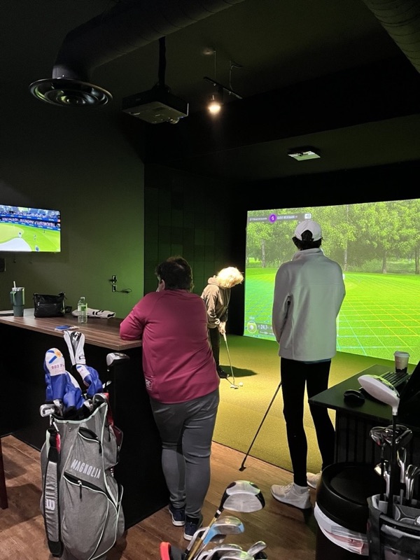 A golfer putting on the simulator while friends watch from the bar