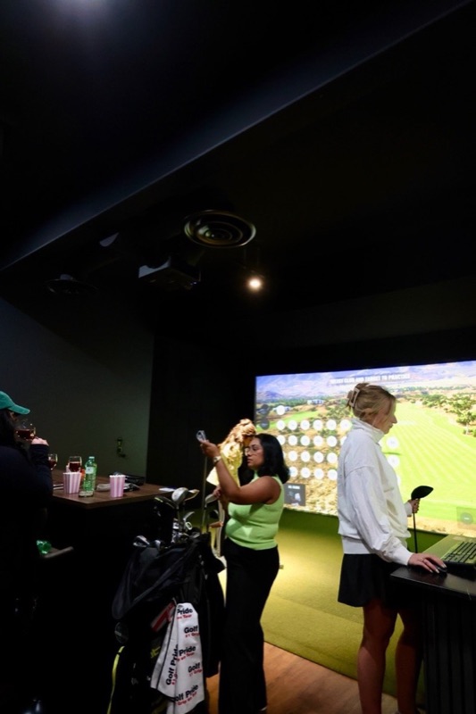 Golfers picking a practice target on the TrackMan screen, drinks on the high-top