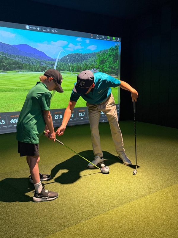 The coach showing a junior golfer how to hold the club in front of the TrackMan screen