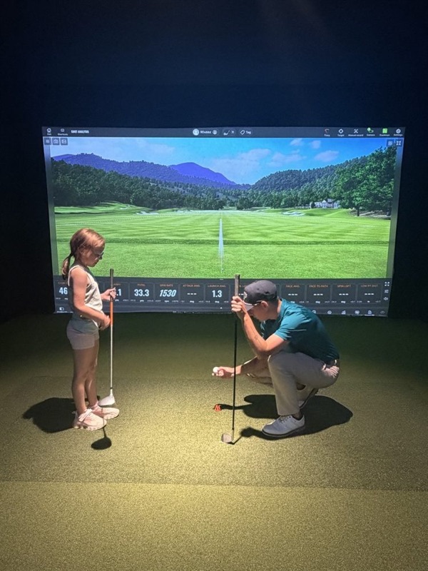 The coach kneeling beside a young golfer to set up her alignment sticks