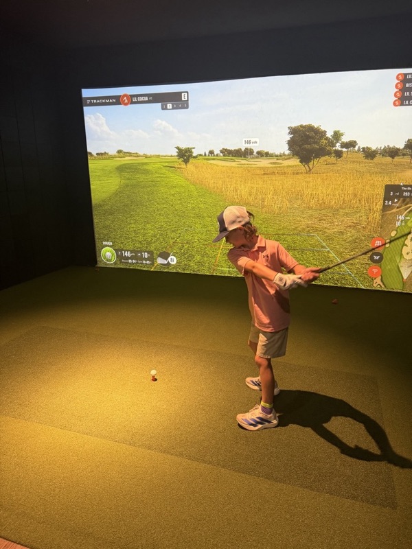 A junior golfer in a cap lining up an 8 iron on a TrackMan course