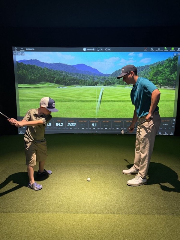 A junior golfer swinging while the coach watches from beside him