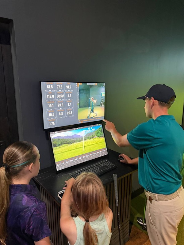 The coach walking two young golfers through their swing data on the bay screen