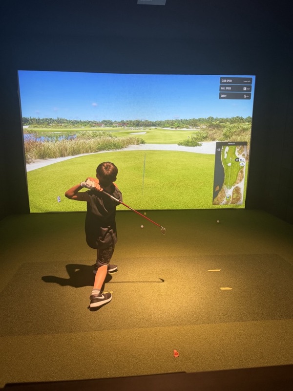A young golfer following through on a wedge on a TrackMan course