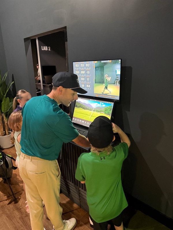 The coach and a junior golfer reviewing a swing video on the bay screen